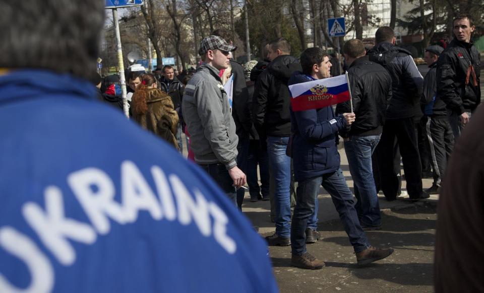 A man holds a Russian flag as people gather outside the Parliament building in Simferopol, Ukraine, Saturday, March 1, 2014. The discord between Russia and Ukraine sharpened Saturday when the pro-Russian leader of Ukraine's Crimea region claimed control of the military and police and appealed to Russia's president for help in keeping peace there. (AP Photo/Ivan Sekretarev)