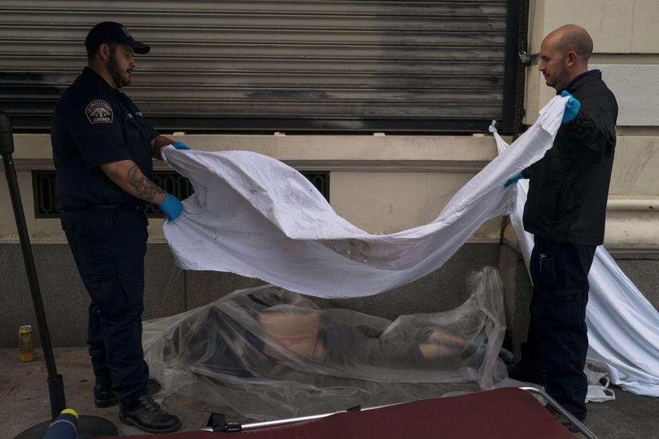 Two men use a white sheet to cover the body of a homeless man found dead on an L.A. sidewalk.