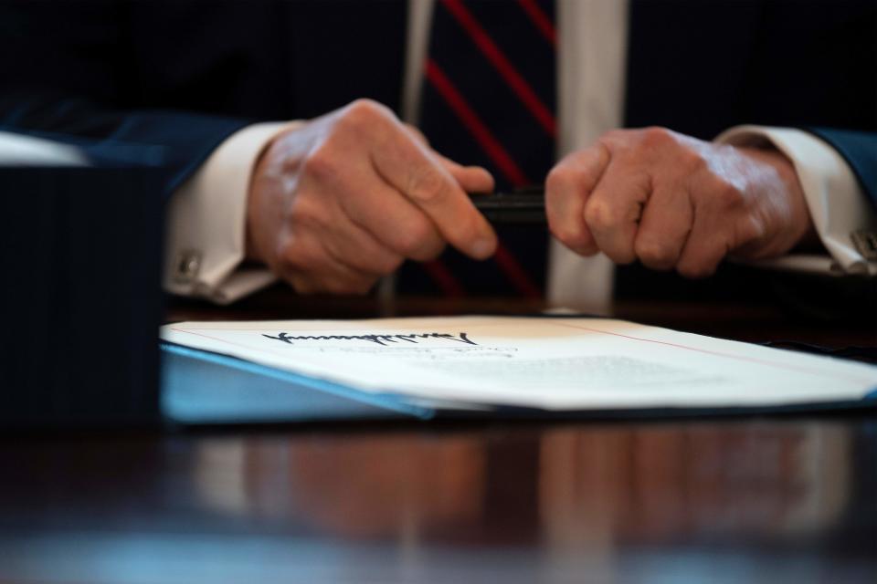 US President Donald Trump signs the CARES act, a $2 trillion rescue package to provide economic relief amid the coronavirus outbreak, at the Oval Office of the White House on March 27, 2020. - After clearing the Senate earlier this week, and as the United States became the new global epicenter of the pandemic with 92,000 confirmed cases of infection, Republicans and Democrats united to greenlight the nation's largest-ever economic relief plan. (Photo by JIM WATSON / AFP) (Photo by JIM WATSON/AFP via Getty Images)