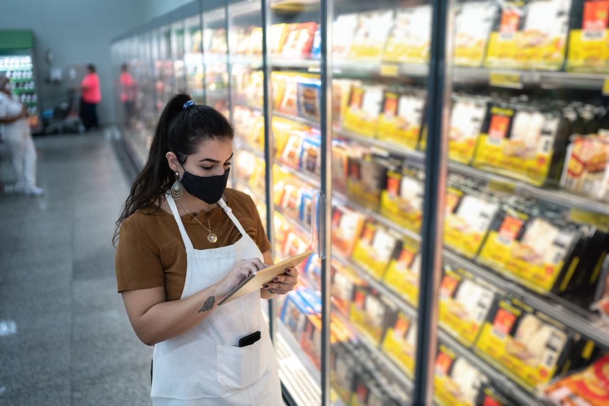 Young woman wearing face mask using digital tablet to check products in a supermarket