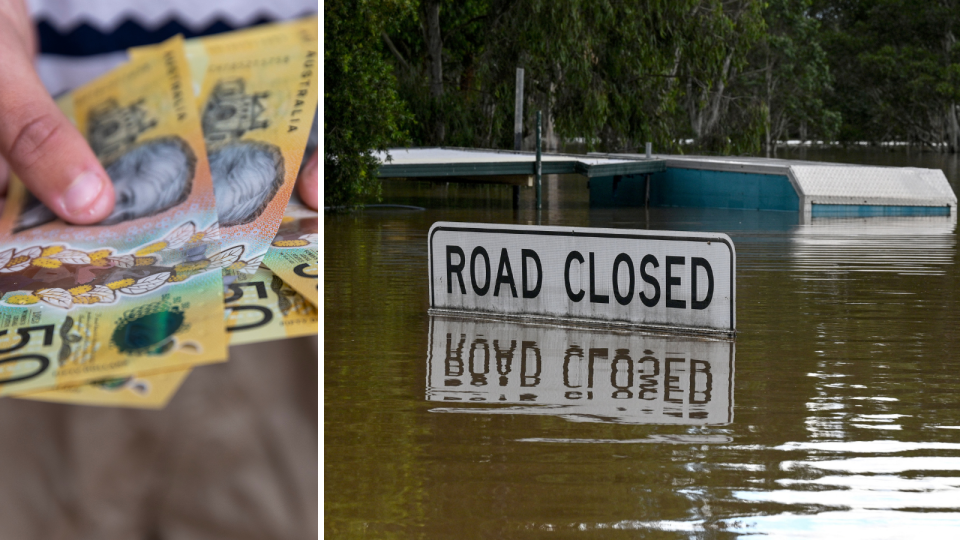 A person holds out Australian $50 notes and a 'road closed' sign underwater due to floods.