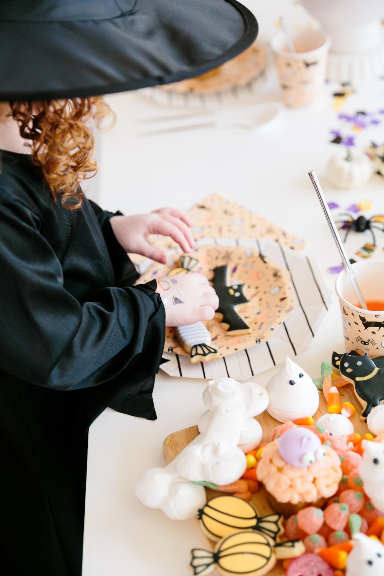 little girl in a witch costume reaching for cookies