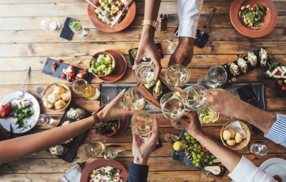 Image of people eating at table and toasting with wine.