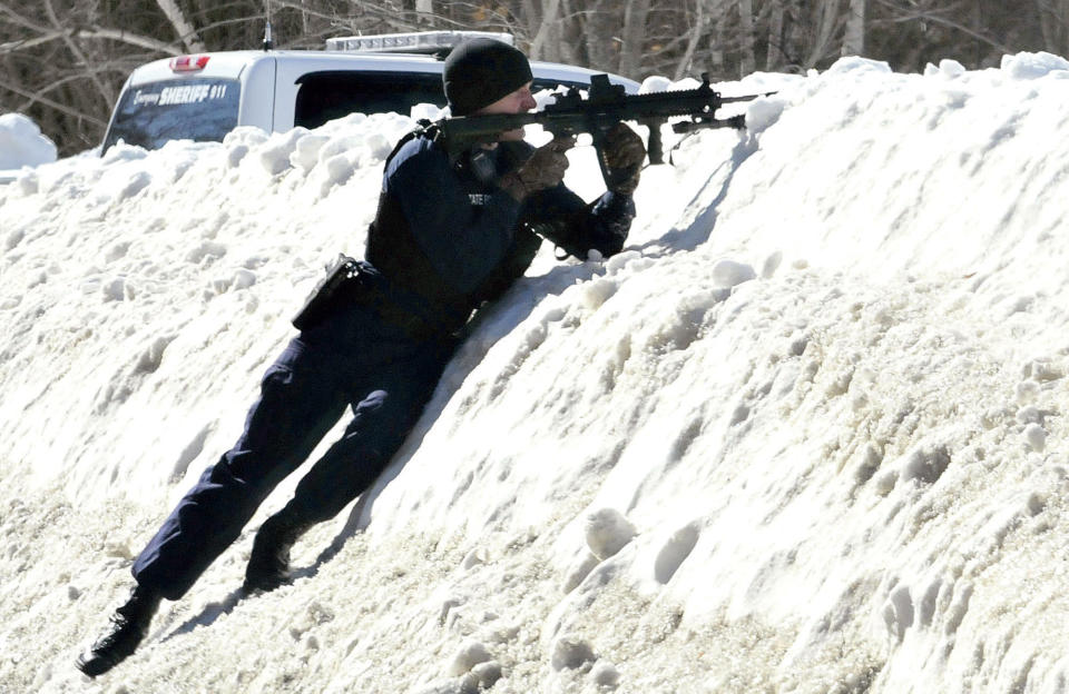 In this Tuesday, March 18, 2014 photo, trooper Scott Duff trains his rifle toward the home of Michael Smith in Norridgewock, Maine. Officers descended on Smith's home after members of a tree removal crew he'd told to clear off his property reported that he had a gun. The "gun" the tree crew had seen on Smith actually was a life-sized tattoo of a handgun on his stomach. (AP Photo/Morning Sentinel, David Leaming)