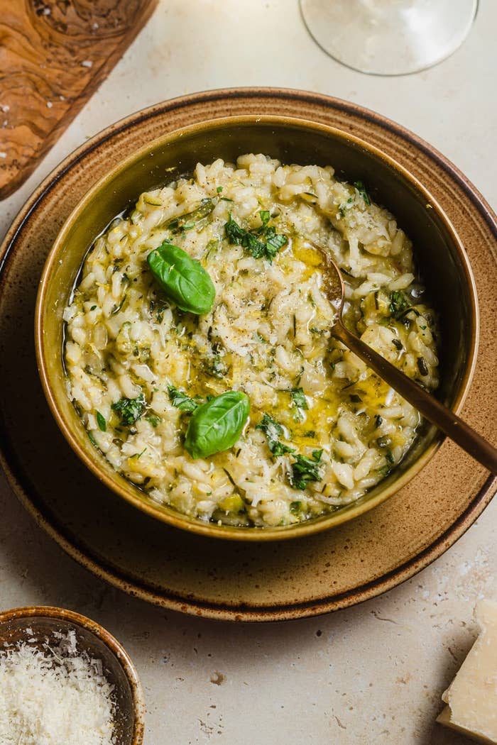 Bowl of creamy risotto garnished with basil leaves, accompanied by a glass of white wine and a small bowl of grated cheese
