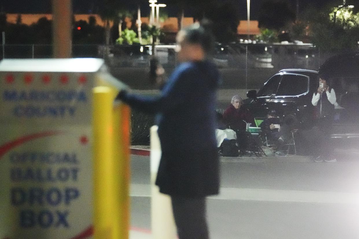 A group of people watch a woman deposit a ballot at the Maricopa County early ballot drop box on Oct. 24, 2022, in Mesa.