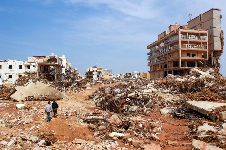 Men walk past debris of buildings caused by flash floods in Derna, eastern Libya, on September 11, 2023. / Credit: AFP via Getty Images