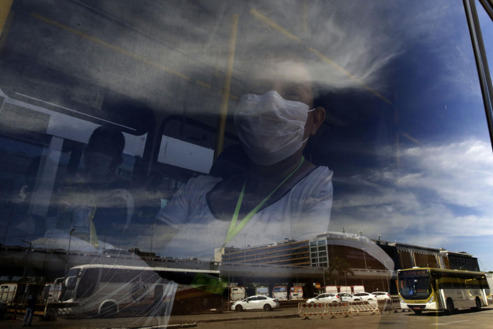 A woman peers from behind a bus window parked at a bus station in Brasilia, Brazil, Monday, May 4, 2020. The state government mandated that commuters using public transportation must wear face masks starting Monday to help contain the spread of the new coronavirus. (AP Photo/Eraldo Peres)