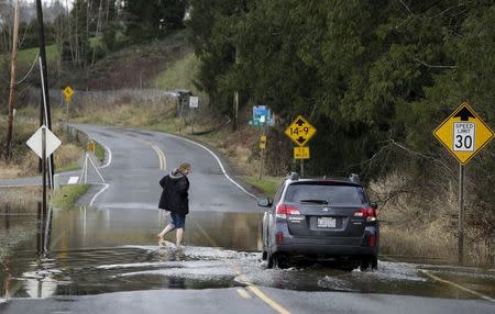 A woman walks through flood waters of the Snoqualmie River as a car drives through on Ames Lake Carnation Road NE during a storm in Carnation, Washington December 9, 2015. REUTERS/Jason Redmond