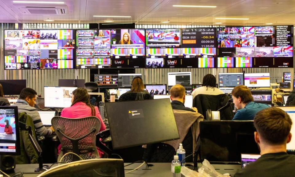 The GB News control room in west London. A view from the back of people working on computers with a bank of TV screens along the far wall.