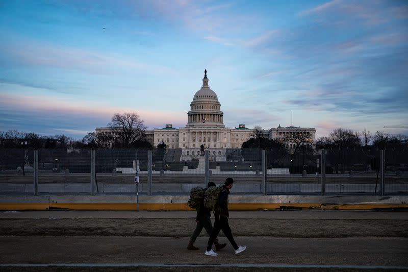People walk past protective fencing surrounding the U.S. Capitol, as the sun sets in Washington