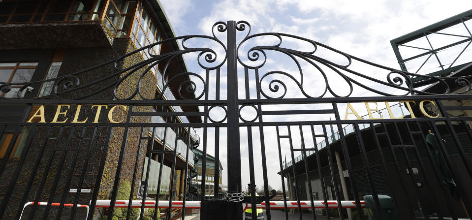 FILE - In this April 1, 2020, file photo, a security guard stands inside the main gates to Wimbledon in London, after the Wimbledon tennis championships was cancelled due to the coronavirus. A year after the worldwide coronavirus pandemic stopped all the games in their tracks, the aftershocks are still being felt across every sector. (AP Photo/Kirsty Wigglesworth, File)