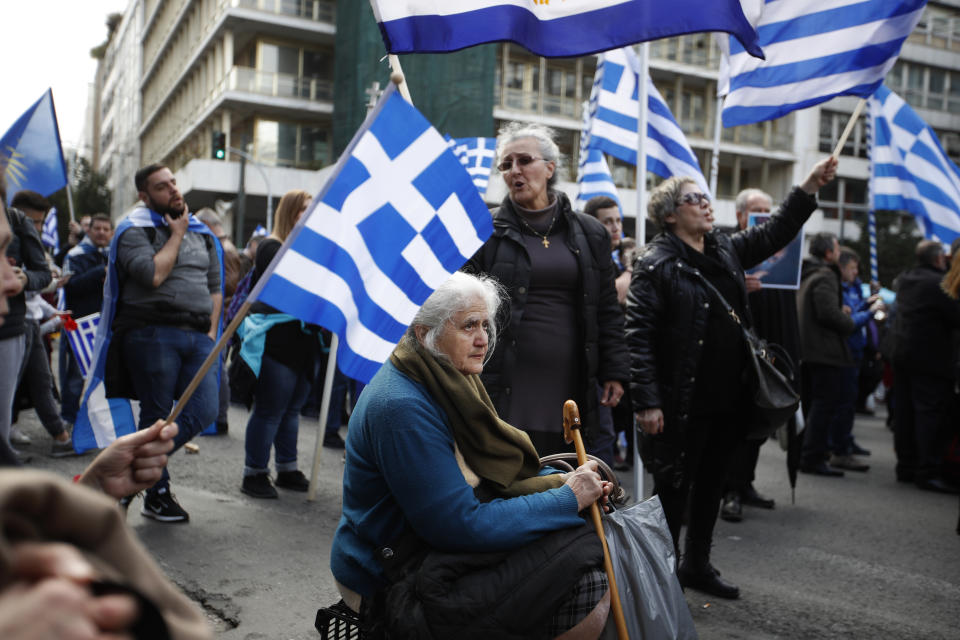 A woman sits down as others hold Greek flags during a rally in Athens, Sunday, Jan. 20, 2019. Greece's Parliament is to vote this coming week on whether to ratify the agreement that will rename its northern neighbor North Macedonia. Macedonia has already ratified the deal, which, polls show, is opposed by a majority of Greeks. (AP Photo/Thanassis Stavrakis)