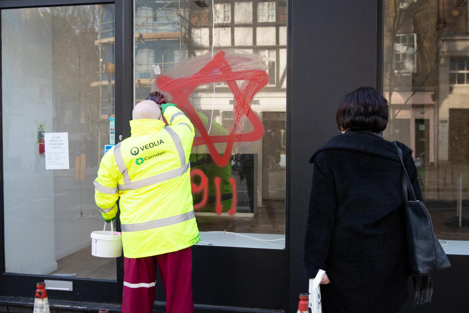 A council cleaner removes anti-semitic graffiti in the form of numbers, 9 11, and a Star of David, on a shop window in Belsize Park, North London.