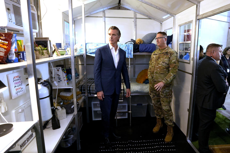 California Gov. Gavin Newsom, left, accompanied by Major General Matthew Beevers, the Adjutant General of the California Military Department, looks over a prototype of one of the small homes displayed at a news conference where Newsom announced plans plans to build 1,200 small homes across the state to reduce homelessness, during the first of a four-day tour of the state in Sacramento Calif., on Thursday, March 16, 2023. (AP Photo/Rich Pedroncelli)