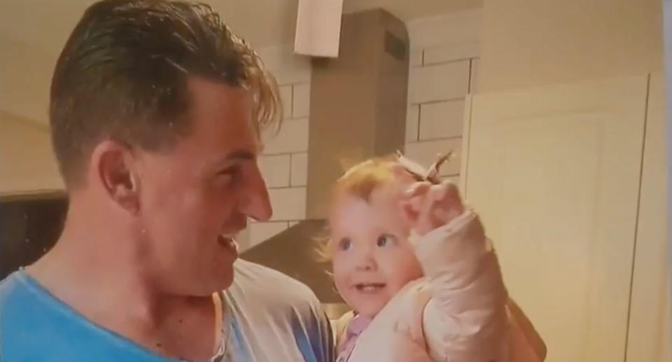 Anthony Clark in a blue T-shirt pictured with his granddaughter inside a kitchen. 