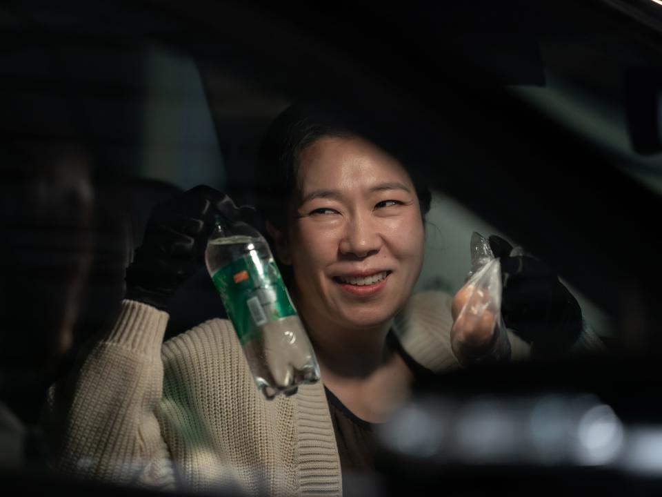 kang hyeon-nam in the glory. she is a middle aged woman sitting in a car, smiling while holding up a drink in a plastic bottle