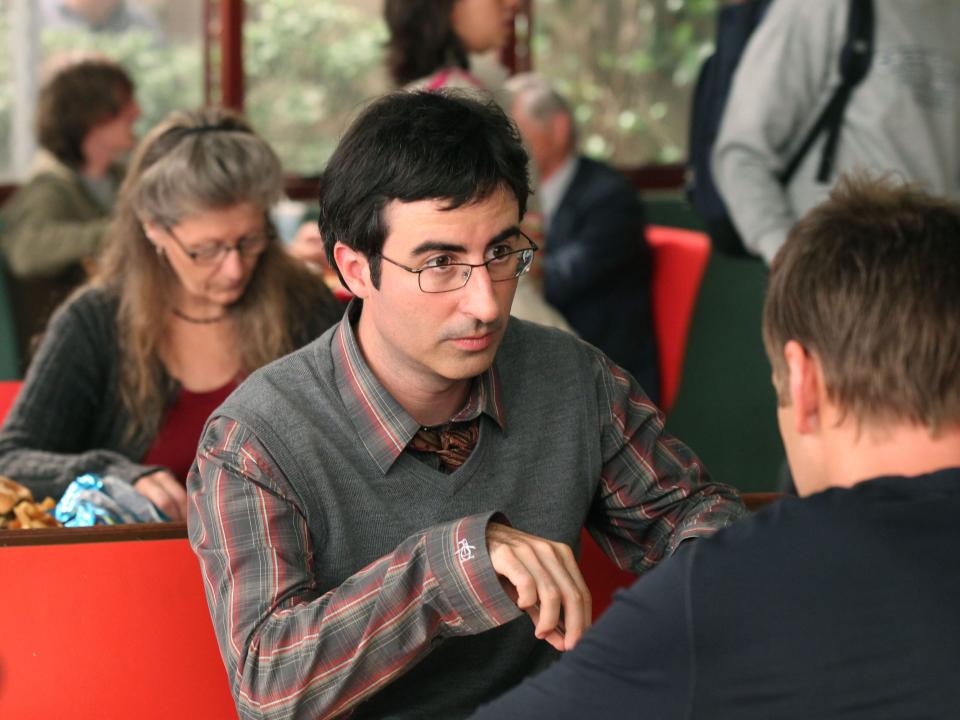 John Oliver as Professor Ian Duncan sits at a cafeteria table in "Community."