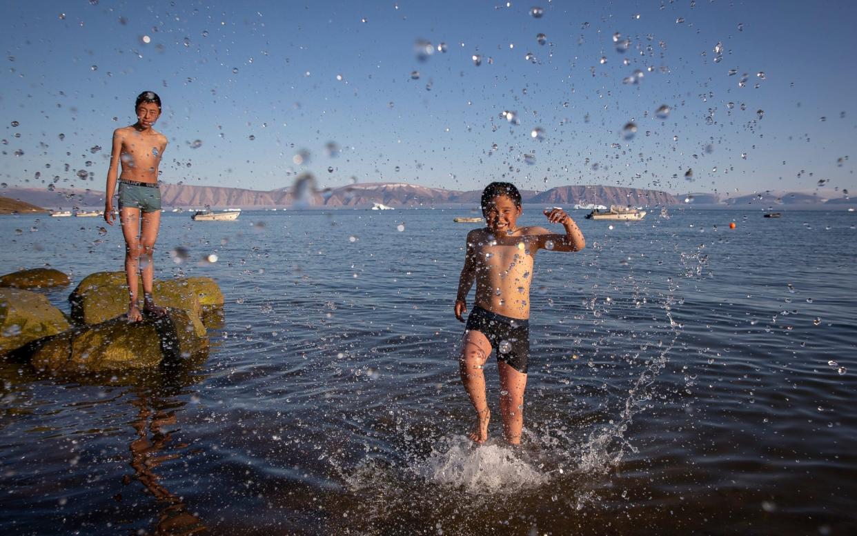 Teenage boys pictured enjoing the recent heatwave by taking a dip in the sea in Qaanaaq, one of Greenland's most northernly towns and settlements - Daily Mirror