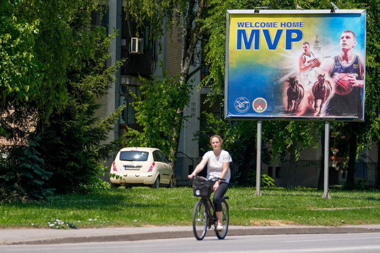 A woman rides a bicycle past a billboard showing Denver Nuggets center Nikola Jokic in his hometown of Sombor, Serbia, on June 18, 2023.<span class="copyright">Darko Vojinovic—AP</span>