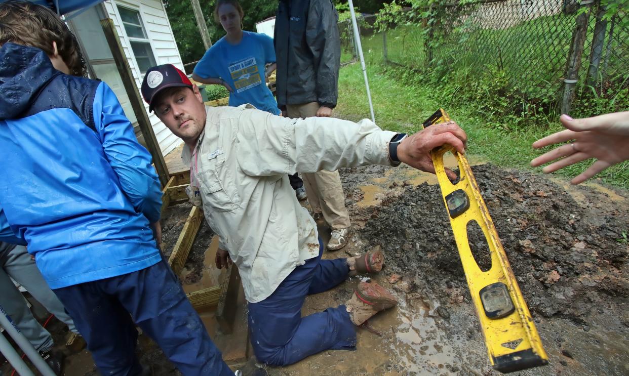 Pastor Travis Allen, with Carolina Cross Connections, is handed a level as he shows a group of teens how to construct a ramp at a home on South Marietta Street in the rain Thursday morning, June 22, 2023.