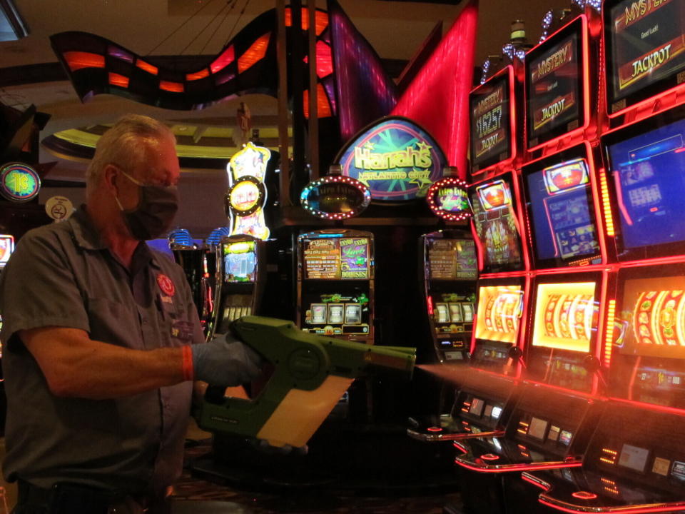 Steven Ford, a worker at Harrah's casino in Atlantic City, N.J., sprays slot machines with disinfectant Wednesday, July 1, 2020, as the casino prepared to reopen after 3 1/2 months of being shut down due to the coronavirus. Five of Atlantic City's casinos will reopen on Thursday, while three others, including Harrah's, will open Friday. (AP Photo/Wayne Parry)