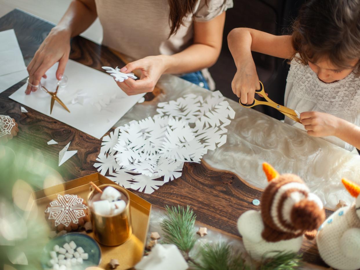Little cute girl and young beautiful woman cut snowflakes from white paper