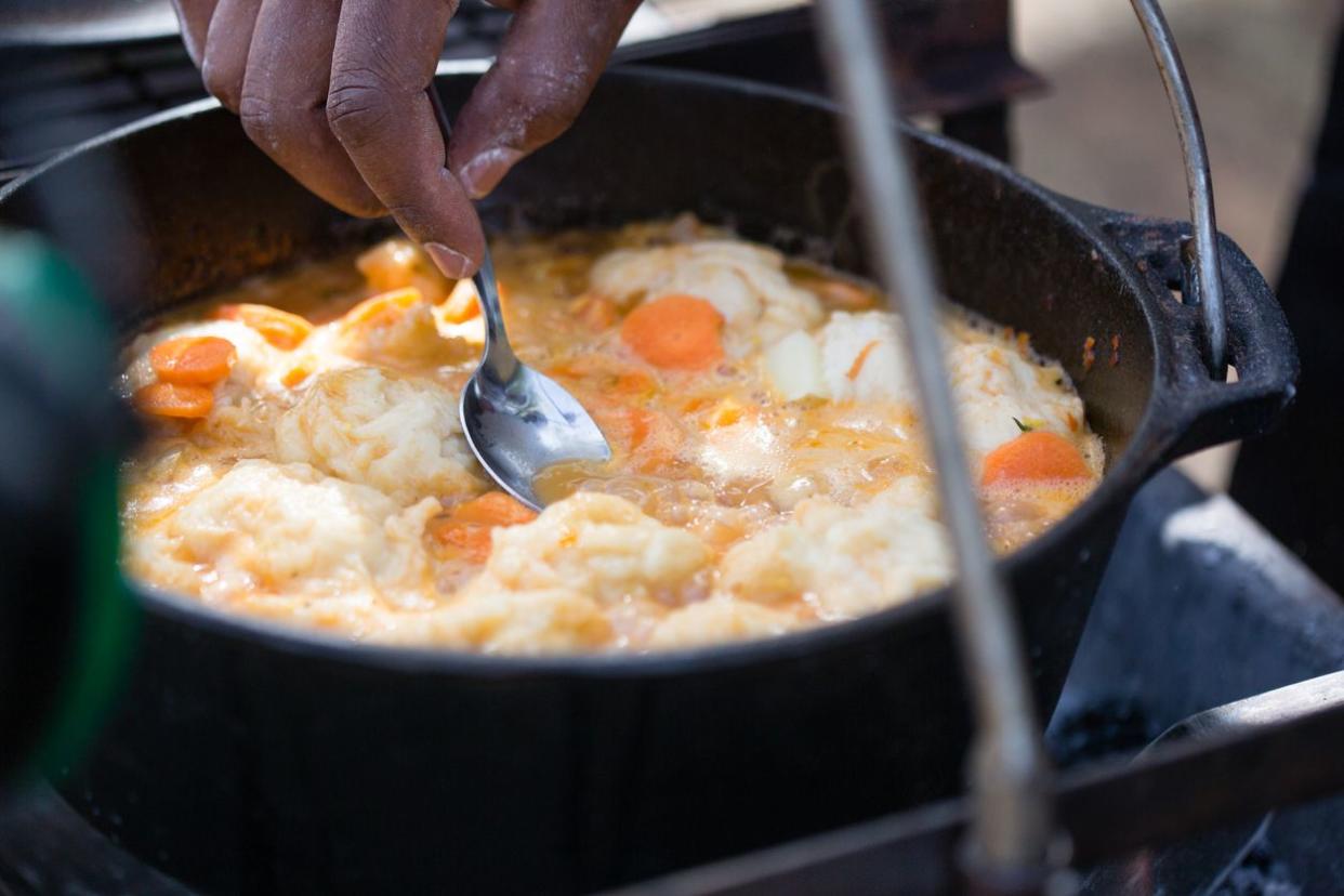 A horizontal composition of a cast-iron pot filled with a vegetable stew and topped with dumplings, a dough that absorbs the sauce and juices of the stew.