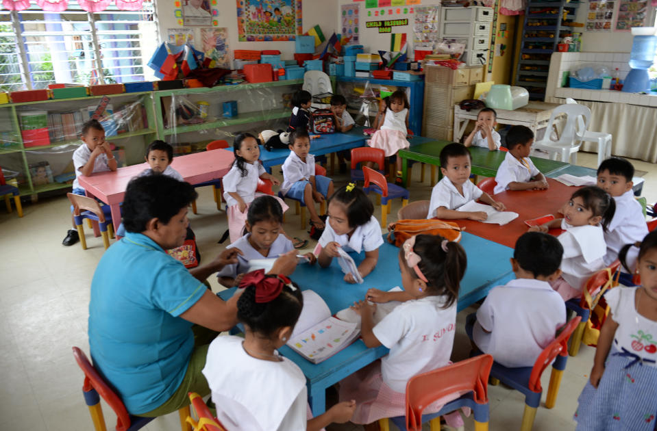 Los niños escuchan a sus maestros en una guardería, junto a la casa ahora abandonada (atrás) que solía transmitir actos sexuales en vivo de niños a pedófilos en Filipinas. Foto: TED ALJIBE / AFP / Getty Images.