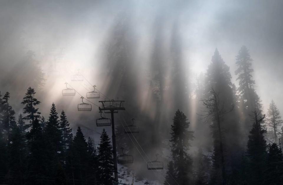 Sun rays break through fog and trees at Palisades Tahoe as empty lifts make their way up the mountain on Thursday, Dec. 21, 2023. Many Tahoe-area ski resorts have limited runs open due to a lack of snow and warmer temperatures.