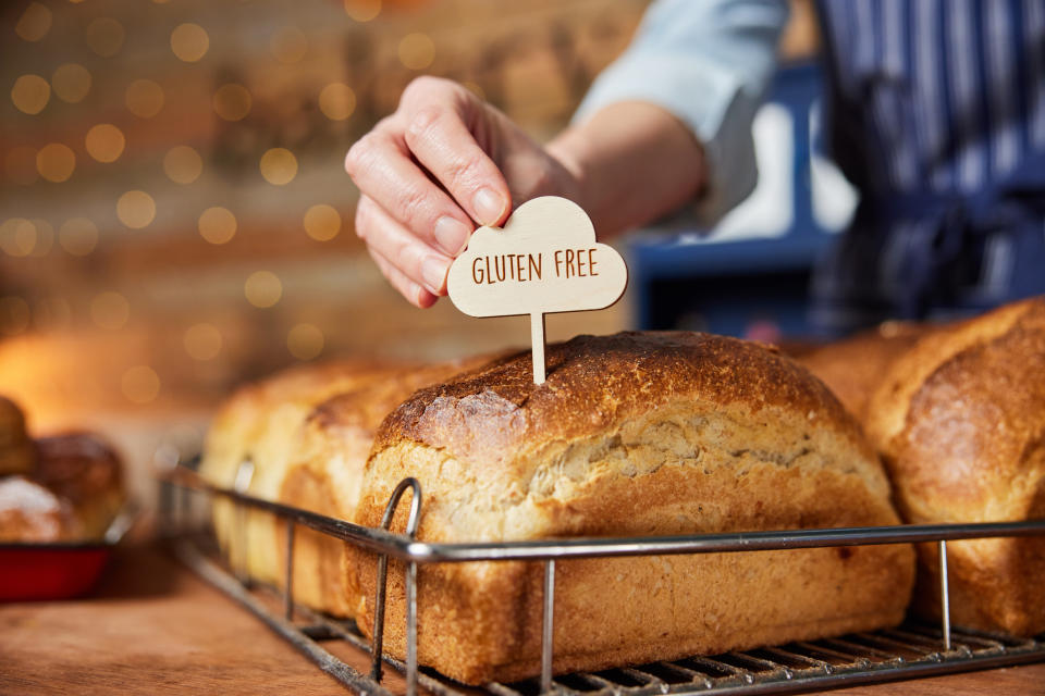 Hand placing a "gluten-free" sign on freshly baked loaves of bread in a bakery display