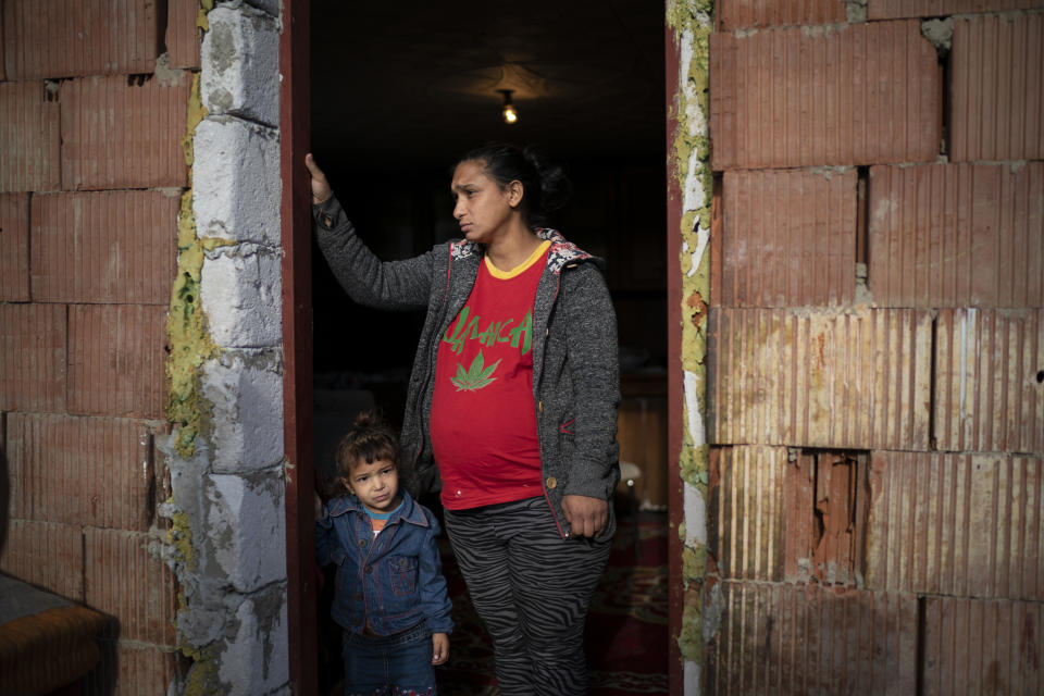 In this Nov. 14, 2018, photo, Jarmila Noskova, 33, stands at the entrance of her house with her daughter in Podhorany village near Kezmarok, Slovakia. Noskova, a Roma woman now pregnant with her seventh child, said she cried for days every time she was forced to remain in the hospital after birth, terrified the hospital would alert the police if she left. (AP Photo/Felipe Dana)