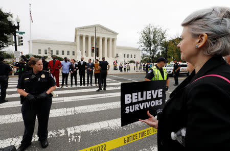 A demonstrator with a sign reading "Believe Survivors" watches as other protestors are arrested by U.S. Capitol police for blocking the street in front of the U.S. Supreme Court while demonstrating against the confirmation of Supreme Court nominee judge Brett Kavanaugh on Capitol Hill in Washington, U.S., October 5, 2018. REUTERS/Yuri Gripas