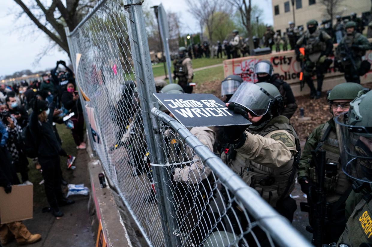 A law enforcement officer tosses a demonstrator's sign that reads "Justice for Wright" back over a perimeter fence during a protest over Sunday's fatal shooting of Daunte Wright during a traffic stop, outside the Brooklyn Center Police Department on Wednesday, April 14, 2021, in Brooklyn Center, Minn.