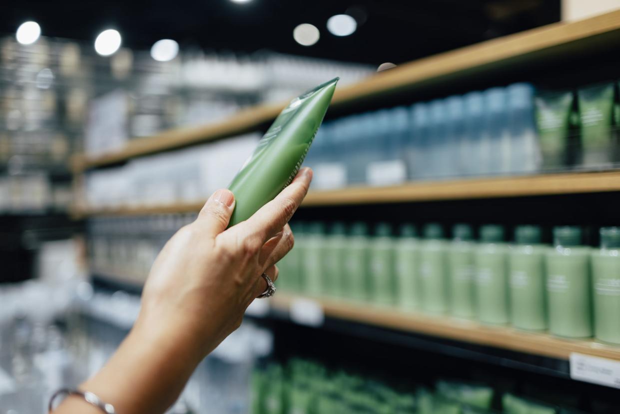 A cropped photo of an anonymous Caucasian woman holding a tube of a hand cream while shopping at a store.