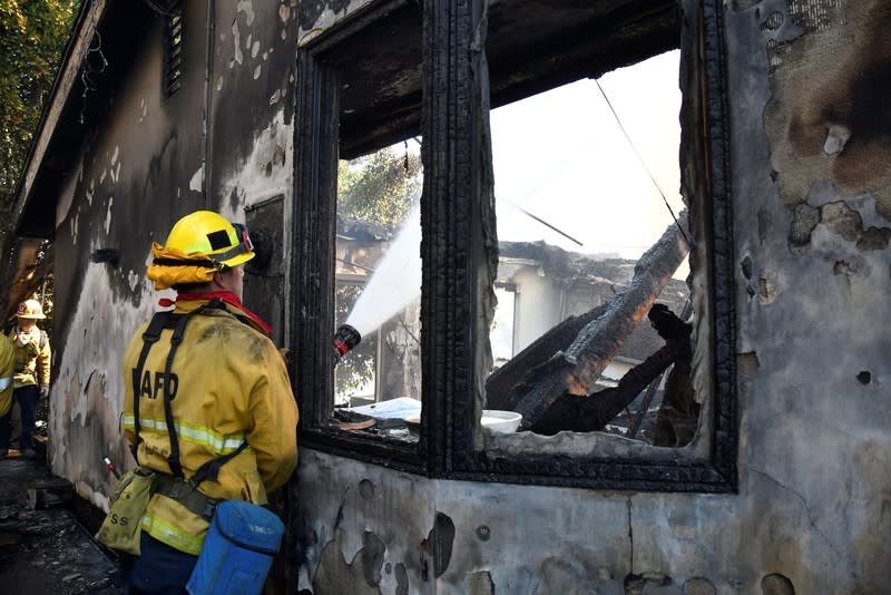 A firefighter douses water on a house after it was burned by the wind-driven Getty Fire in West Los Angeles, California