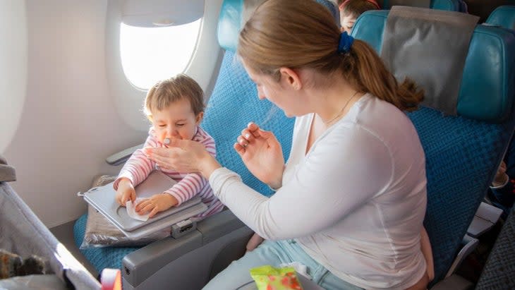 A mom attempts to cover her toddler's sneeze as they sit next to each other on an airplane.