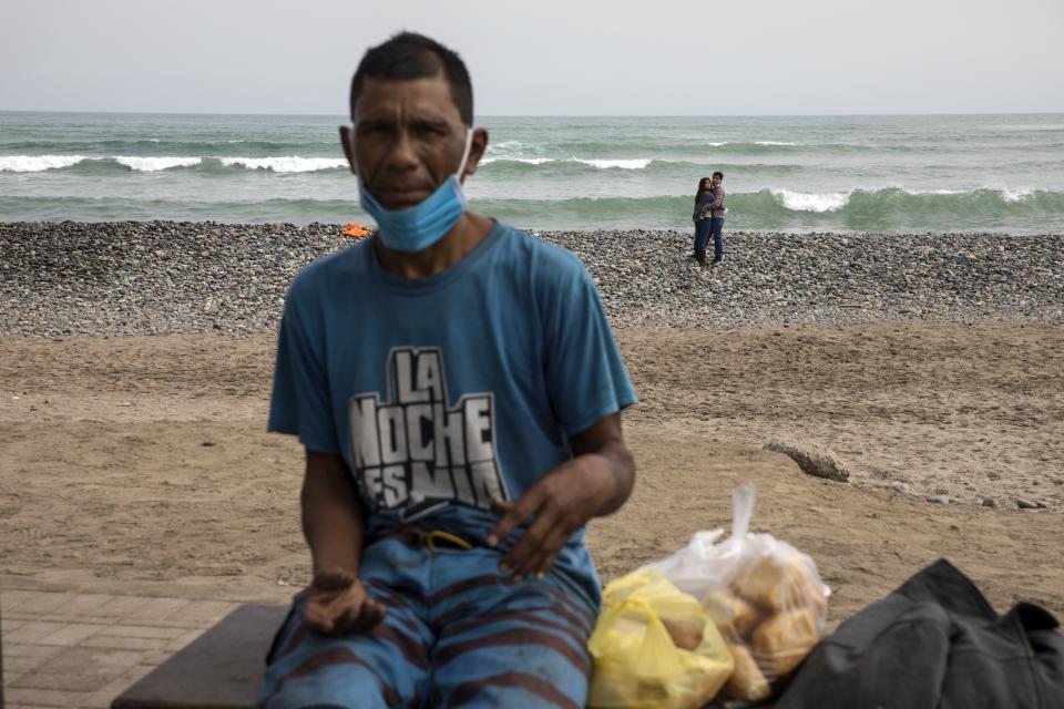 A couple embraces, background, while homeless Gustavo Castaneda rests on a bench near the Pacific Ocean on the coast of Lima, Peru, Friday, June 26, 2020, amid the coronavirus pandemic. (AP Photo/Rodrigo Abd)