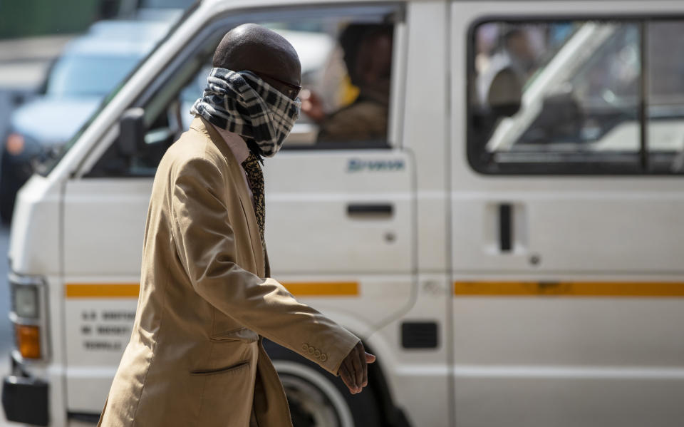 A man using a scarf to cover his face walks along a downtown street Johannesburg, South Africa, Monday, March 16, 2020. South African President Cyril Ramaphosa declared a national state of disaster. Ramaphosa said all schools will be closed for 30 days from Wednesday and he banned all public gatherings of more than 100 people. South Africa will close 35 of its 53 land borders and will intensify screening at its international airports. For most people, the new COVID-19 coronavirus causes only mild or moderate symptoms. For some it can cause more severe illness. (AP Photo/Themba Hadebe)