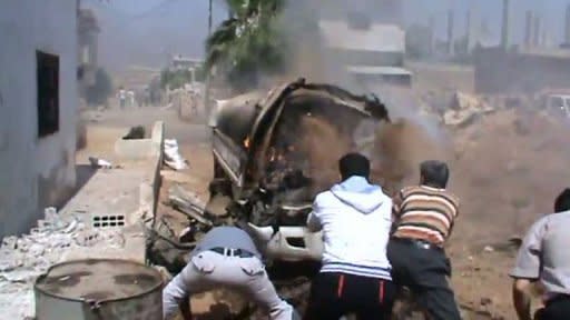 An image taken from a video uploaded on YouTube on July 20 shows men throwing sand to extinguish a burning vehicle following the purported shelling of the town of Daraa by Syrian government forces