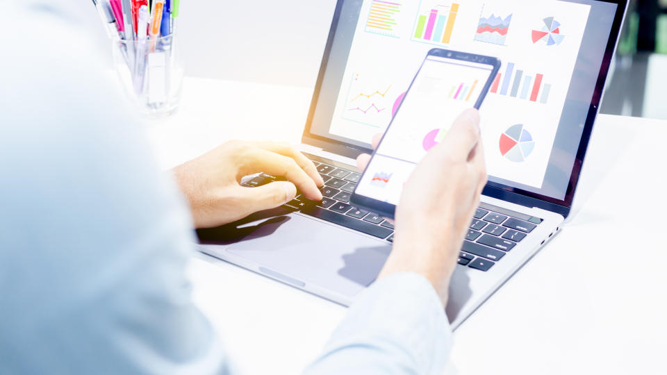 Businessman at work with laptop and smartphone with computer screen showing graphics and charts.