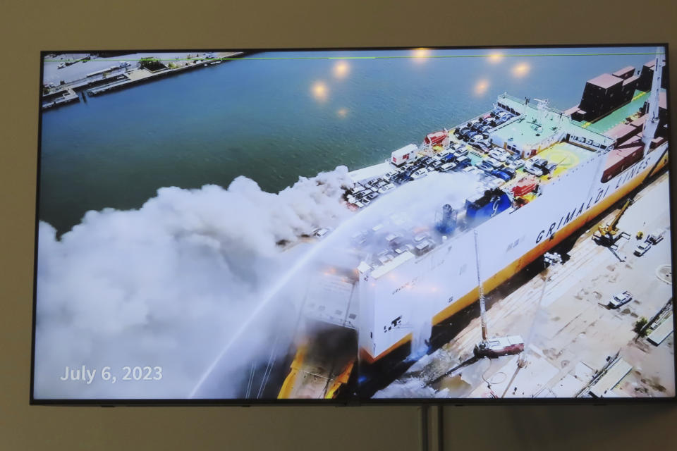 A photo displayed on a video monitor in Union,N.J., Wednesday, Jan. 10, 2024 shows a burning cargo ship in Newark N.J. on July 5, 2023. Federal investigators are conducting hearings into the blaze that killed two Newark, N.J. fire captains. (AP Photo/Wayne Parry)