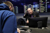 In this Nov. 18, 2019, photo, Sportsbook shift manager Stuart Norsell, right, assists a patron, left, in the sports betting area of Twin River Casino in Lincoln, R.I. Legalized sports betting's rapid march across the U.S. could face some bigger tests in 2020. Less than two years after a U.S. Supreme Court ruling opened the door to sportsbooks outside Nevada, they have been legalized in states that are home to about one-third of the nation's population. (AP Photo/Steven Senne)