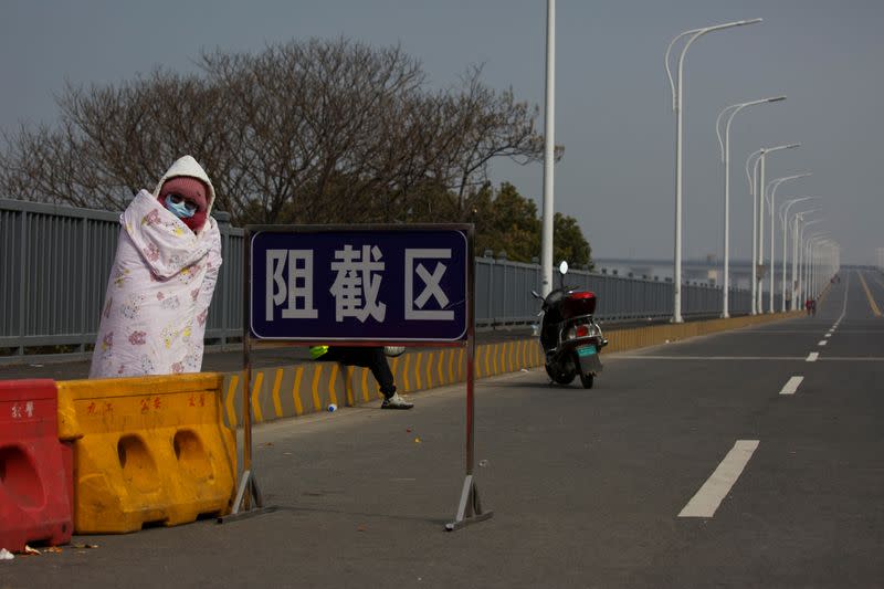 A leukaemia patient who arrived from Hubei province waits next to a sign that reads 'exclusion zone' for permission to cross a checkpoint in Jiujiang
