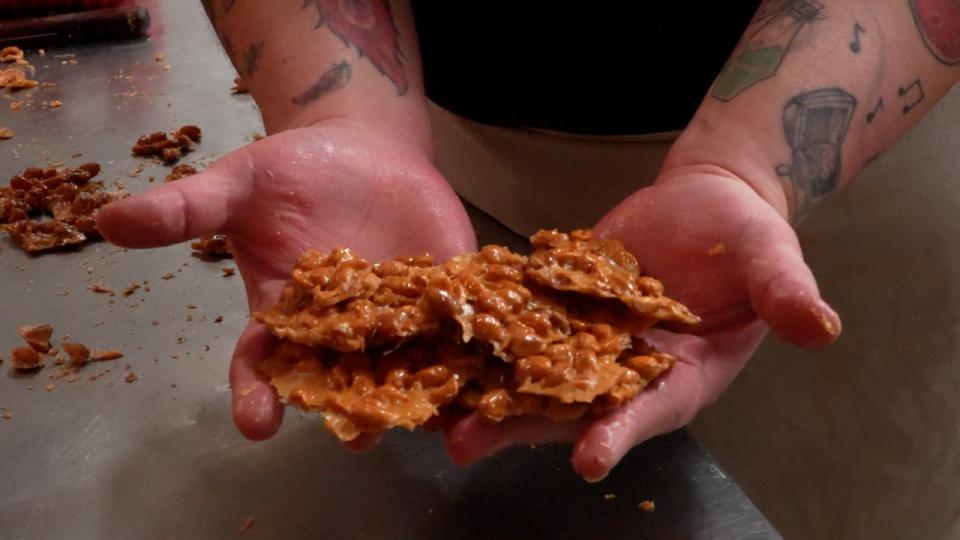 Brenda Priest shows off some of her handmade peanut brittle, using techniques shown to her by Murray Lawlor, who founded the candy shop back in 1975 and developed his craft over decades. 