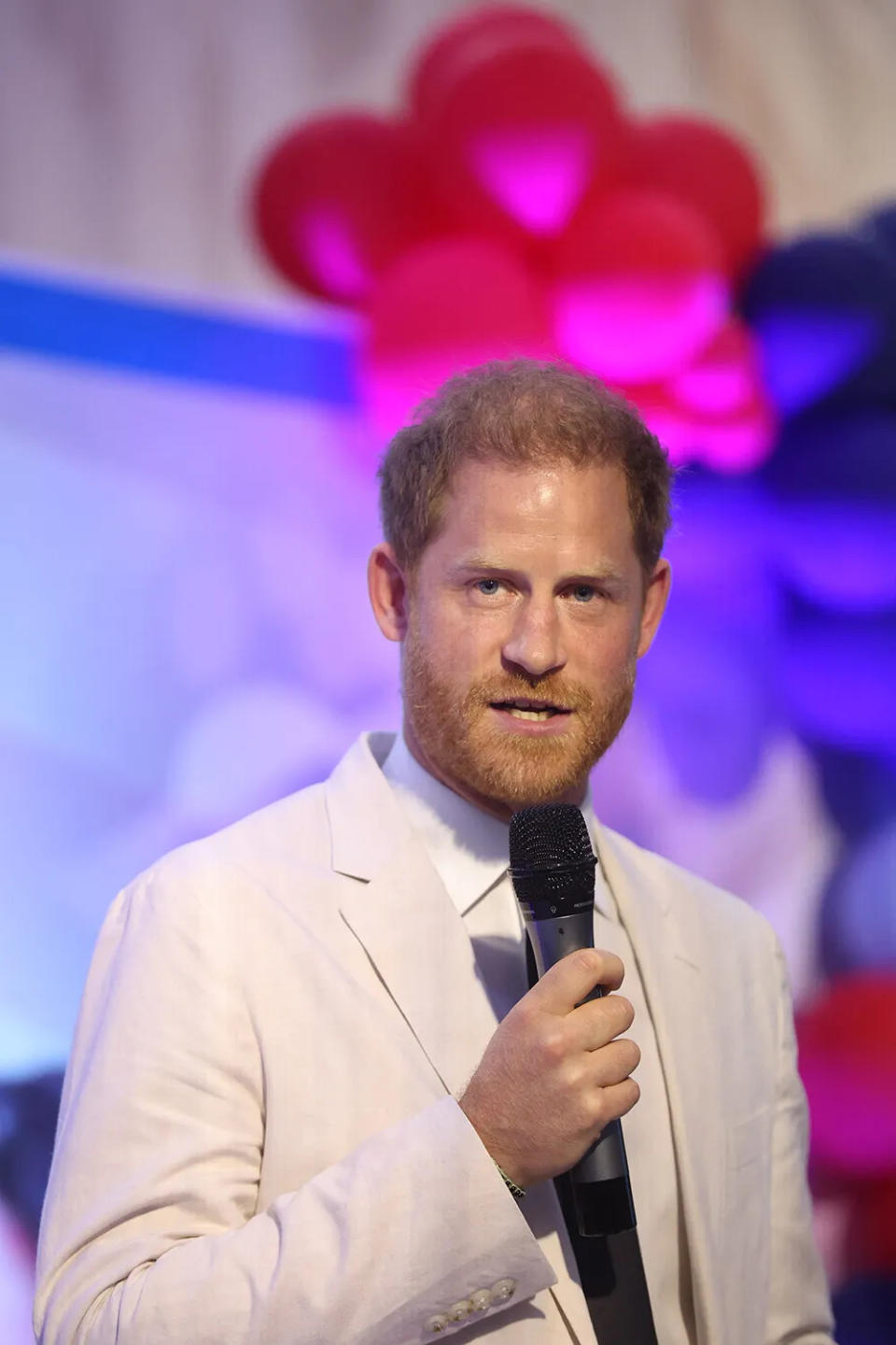 Prince Harry speaking to a mic wearing an off-white suit