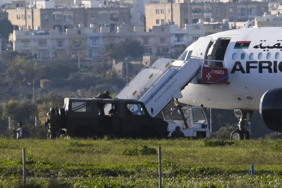 This Friday, Dec. 23, 2016 photo shows a man with raised arms, left, standing next to an Afriqiyah Airways plane from Libya stopped on the tarmac at Malta's Luqa International airport. Two hijackers diverted a Libyan commercial plane to Malta on Friday and threatened to blow it up with hand grenades, Maltese authorities and state media said. (AP Photo/Jonathan Borg)