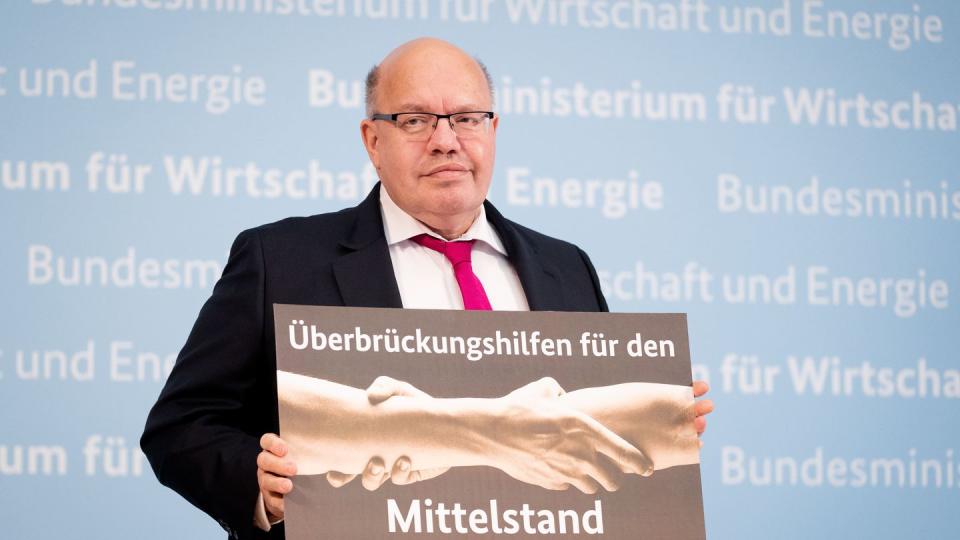 Peter Altmaier (CDU) hält ein Plakat mit der Aufschrift "Überbrückungshilfen für den Mittelstand" in den Händen.