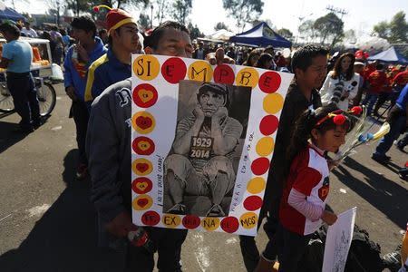 A man holds a poster with a picture of "El Chavo del Ocho", a character created by screenwriter Roberto Gomez Bolanos, as he waits to enter the Azteca stadium for a mass in memory of Gomez Bolanos in Mexico City November 30, 2014. REUTERS/Tomas Bravo