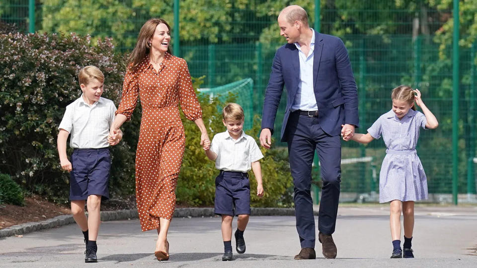 Prince William in a navy blazer and matching pants with a white shirt walking alongside his wife and their three children